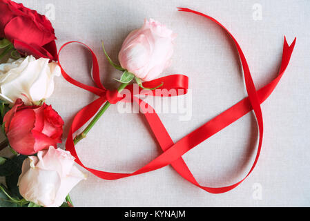 Tag der Frau Bild mit einem rosa mit roter Schleife in Form der Zahl 8, durch rote und weiße Rosen umgeben gebunden Rose, auf einem vintage Stoff Hintergrund. Stockfoto