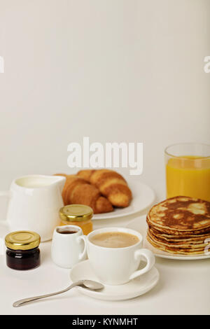 Frühstück - Kaffee mit Croissants, Saft mit Pfannkuchen auf einem weißen Hintergrund. Selektive konzentrieren. Stockfoto