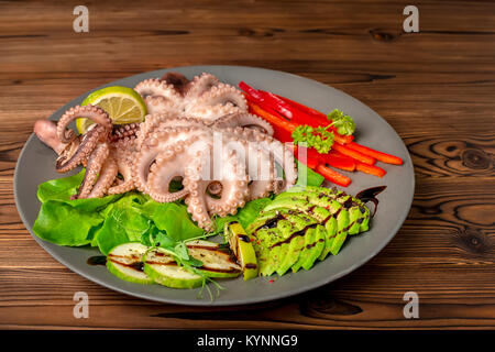 Octopus mit in Scheiben geschnittenen Avocado, Salat, Paprika, Kalk, Gurke und Zweig von Erbse Blätter auf dem Teller serviert, gesunde Bio-Lebensmittel Stockfoto