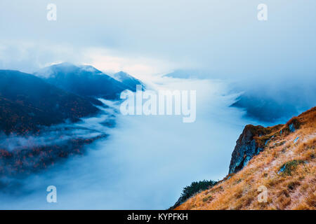 Berglandschaft mit Nebel unter dem Gipfel und Wolken über Ihnen in blauen Farbtönen Stockfoto