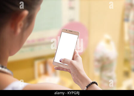 Frau mit Mobiltelefon zum Einkaufen. Isoliert, weißer Bildschirm für Text schreiben oder App mockup. Bekleidungsgeschäft im Hintergrund. Stockfoto