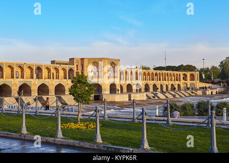 Isfahan, Iran - April 24, 2017: Ein junger Baum auf eine Stadt Rasen mit Kette fechten vor dem Hintergrund der Pol eingezäunt - e Khaju Brücke über den Zayand Stockfoto