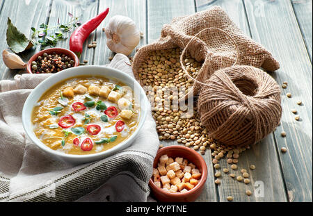Würzige Linsensuppe mit Chili, Knoblauch und Zwiebel auf rustikalen Holztisch. Die Suppe mit Sahne, Chili, Zitronensaft, Croutons und Thymian in Weiß serviert. Stockfoto