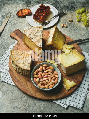 Käseplatte mit Käse Sortiment, grüne Trauben, Brot, Honig und Nüssen über grauer Beton Hintergrund. Partei oder der Sammlung Konzept Essen Stockfoto