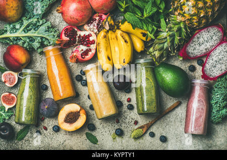 Flachbild-lay von bunten Smoothies in Flaschen mit frischen tropischen Früchten und Superfoods auf konkreten Hintergrund, Ansicht von oben. Gesunde, saubere Essen, vegan, Veg Stockfoto