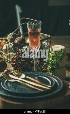 Weihnachten oder Silvester Urlaub Tabelle einstellen. Teller, Besteck, Champagner im Glas, Kerze und Spielzeug festliche Dekorationen über vintahge Tabelle zurück Stockfoto