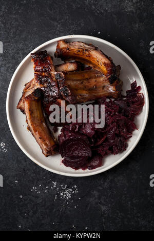 Gegrillte Schweinerippchen mit Balsamico und Honig Soße gekocht, garniert mit Rotwein geschmorten Rotkohl mit Rüben auf weiße Platte. Dunklen rustikalen Bac Stockfoto