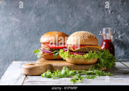 Der hausgemachte Burger im klassischen Brötchen mit Tomaten, Kopfsalat, Rucola, Käse, Zwiebel auf Holz das Brett über weiße Holzbrett Tabelle. Rustikale Stockfoto
