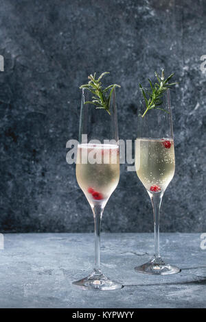 Zwei Gläser Champagner weiß mit roten Beeren serviert und Rosmarin über blaue Textur Hintergrund. Platz kopieren Stockfoto