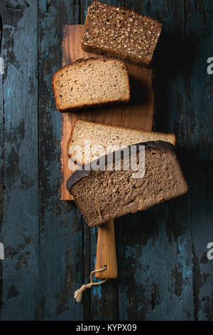 Verschiedene Brote in Scheiben hausgemachtes Roggenbrot Vollkorn und Samen auf Holz Schneidebrett über alten dunklen Hintergrund. Ansicht von oben, Platz. Gesund ea Stockfoto