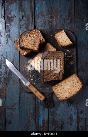 Verschiedene Brote in Scheiben hausgemachtes Roggenbrot Vollkorn und Samen mit Messer am schwarzen Brett über dem alten dunklen Hintergrund. Ansicht von oben, Platz. Stockfoto