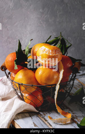 Bio clementinen oder Mandarinen mit Blättern im Korb stehend mit Küchentuch auf weißem Holzbrett Tabelle mit grauen Wand als Hintergrund Reif. Rus Stockfoto