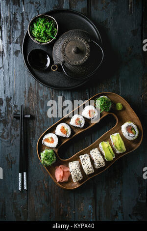 Hausgemachte sushi Brötchen mit Lachs, Sesam und Avocado in Holz Platte serviert mit Rosa eingelegter Ingwer, Sojasauce, Wasabi, Algensalat, Koteletts Stockfoto