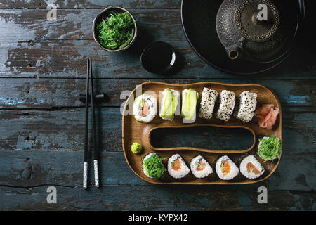 Hausgemachte sushi Brötchen mit Lachs, Sesam und Avocado in Holz Platte serviert mit Rosa eingelegter Ingwer, Sojasauce, Wasabi, Algensalat, Koteletts Stockfoto