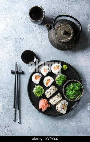 Hausgemachte sushi Brötchen mit Lachs, Sesamsamen in Schwarz mit Rosa eingelegter Ingwer, Sojasauce, Wasabi, Algensalat, Essstäbchen auf gr Stockfoto