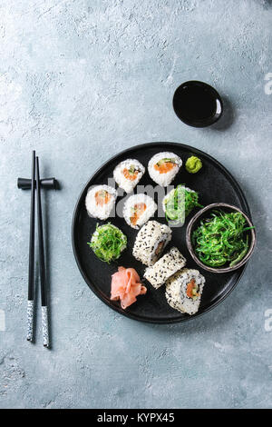 Hausgemachte sushi Brötchen mit Lachs, Sesamsamen in Schwarz mit Rosa eingelegter Ingwer, Sojasauce, Wasabi, Algensalat, Essstäbchen auf gr Stockfoto