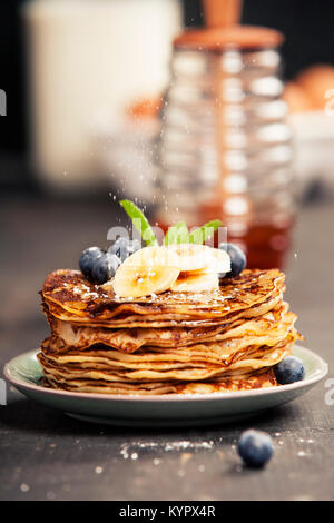 Pfannkuchen mit frischen Bananen, Blaubeeren und Honig auf einem rustikalen Tisch Stockfoto