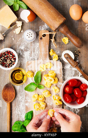 Raw italienische pasta Tortellini mit Zutaten auf Holzbrett. Ansicht von oben Stockfoto