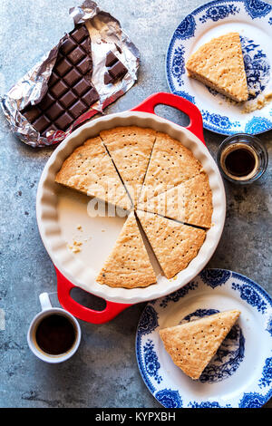 In Scheiben geschnitten Shortbread Cookies in einer Pfanne mit Tasse Kaffee und ein Stück Schokolade auf dem Tisch Stockfoto