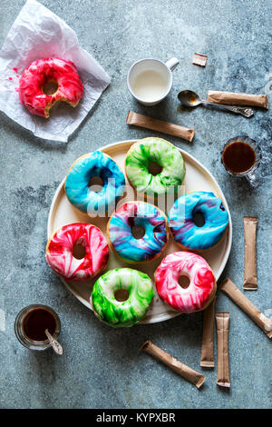 Donuts mit marmorierten Sahnehäubchen auf einem Teller und Tassen auf dem Tisch Stockfoto