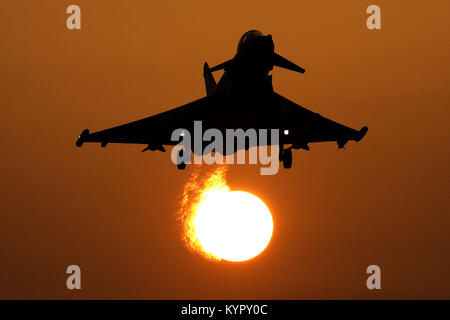 RAF Typhoon silhouetted gegen die untergehende Sonne kehrt in RAF Coningsby an einem nebligen Tag mit der Sonne durch die Jets Auspuff verzerrt. Stockfoto