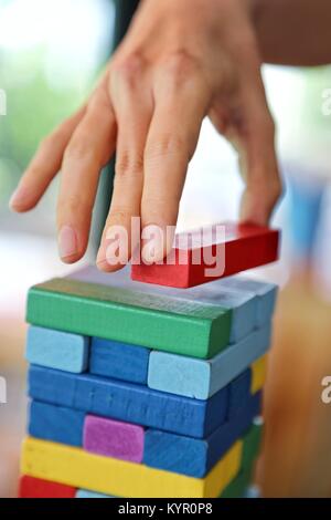 Nahaufnahme der Frau Hand spielen bunte Holzklötze Spiel stack, Jenga, im Morgenlicht, die Spielen und Lernen Hintergrund Konzept Stockfoto