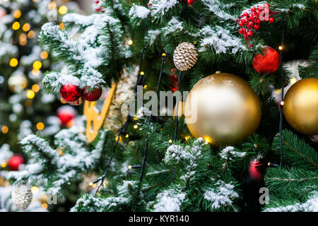 Schnee bedeckt künstlicher Weihnachtsbaum mit roten und gelben Glas ornament Kugeln und elektrischen Lichtern dekoriert. Bunten Hintergrund Stockfoto