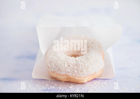 Nahaufnahme eines weißen Donut mit Kokosnuss Topping auf einen hellen Hintergrund innen Papier Lieferung Verpackung. High key Essen Fotografie. Stockfoto