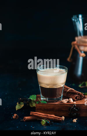 Espresso mit Schaum auf eine Holzkiste mit Kaffeebohnen, arabica Blätter, Zimt und Gewürze auf dunklem Hintergrund. Kaffee brühen in Chemex. Heiße Getränke Stockfoto