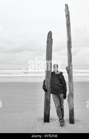 Portrait von älteren Menschen am Strand stehen mit Treibholz Beiträge in den Sand. Ozean im Hintergrund. Schwarz und Weiß Schwarzweiß. Kopieren Sie Platz. Stockfoto