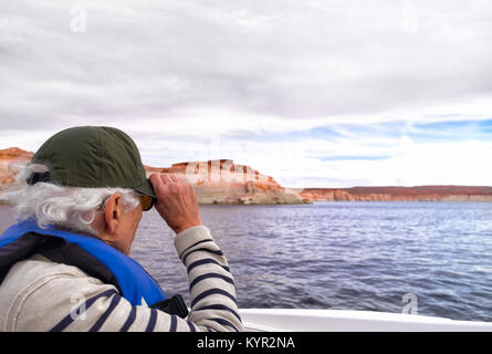 Active Senior auf einem Schnellboot, halten uns an seinen Hut. Er trägt einen diskreten Hörgeräten, leicht hinter seinem Ohr gesehen. Ort: Lake Powell, Arizona Stockfoto