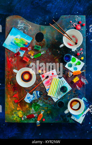 Artist Arbeitsplatz mit leeren Kaffeetassen, Öl und Aquarell Pinsel auf eine bunte Palette, Skizzen und Snacks. Flach mit kopieren. Creati Stockfoto