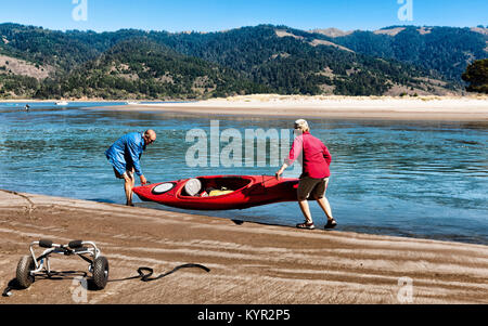 Active Senior Paar heben ein Kajak in das Wasser. Körperliche Aktivitäten helfen Senioren fit, gesund und unabhängig zu bleiben. Lage: Bolinas, Kalifornien Stockfoto