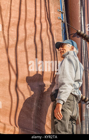 Älterer Mann auf einem Segelboot hilft, die Segel zu hissen. Abenteuer auf einem Großsegler Schoner. Konzept für gesundes Wohnen im aktiven Ruhestand. Stockfoto