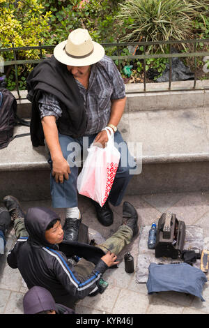 SAN JUAN OSTUNCALCO, GUATEMALA - 24. Juni: Ein unbekannter Mann auf einer Parkbank bekommt Schuh durch ein nicht ermitteltes Kind am San Juan Ostuncalco cen glänzte Stockfoto