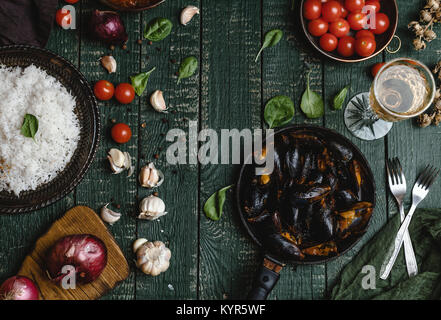 Blick von oben auf die gekochten Muscheln mit Schalen in Pfanne mit Tomaten, Kräuter und Wein am Tisch serviert Stockfoto