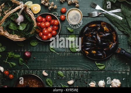 Blick von oben auf die gekochten Muscheln mit Schalen in Pfanne mit Tomaten, Kräuter und Wein auf rustikalen Tisch serviert Stockfoto