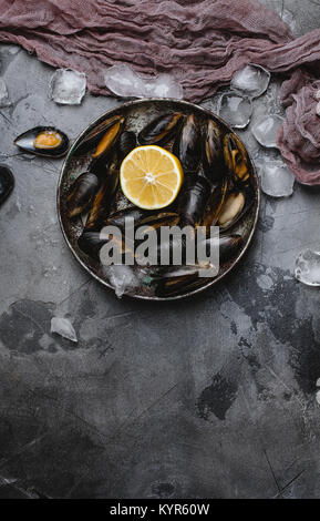 Blick von oben auf die leckeren Muscheln mit Muscheln und Zitrone auf vintage Platte und Eiswürfel auf Grau Stockfoto