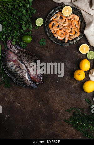 Frischen, rohen Fisch, Garnelen, Kräuter mit Zitronen und Tischdecke auf dunklen Tischplatte Stockfoto