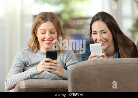 Vorderansicht des zwei glückliche Mitbewohner mit zwei Smartphones auf einer Couch im Wohnzimmer zu Hause liegen Stockfoto
