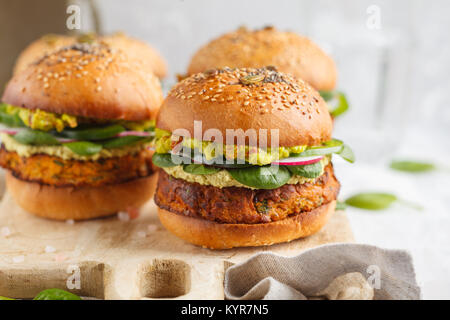 Gesunde gebackene süsse Kartoffel Burger mit Vollkorn Brötchen, Guacamole, vegane Mayonnaise und Gemüse auf einem Brett. Vegetarisches Essen Konzept, Licht backgrou Stockfoto