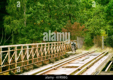 Alten, verlassenen Eisenbahnbrücke über den Fluss in Polen; vintage Motorrad im Hintergrund. Vintage industrielle Landschaft Stockfoto