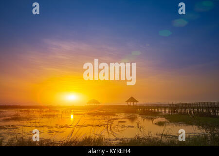 Sonnenuntergang mit Lens Flare über Sumpf mit hölzernen Pavillon und Brücke im ländlichen Thailand Stockfoto