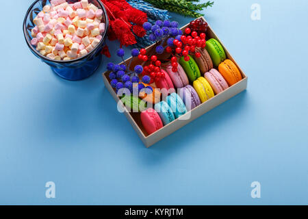 Bunte makronen in einer Geschenkbox und Marshmallow in Vase auf blauem Hintergrund. Süße macarons und Blumen. Franch Süßigkeiten Stockfoto