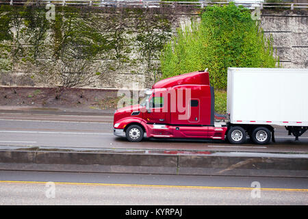 Eine Seitenansicht eines großen, hellen roten American Semi Truck mit angehobener Kabine und Schlafplatz für den Fahrer bei der Beförderung von Gütern Stockfoto