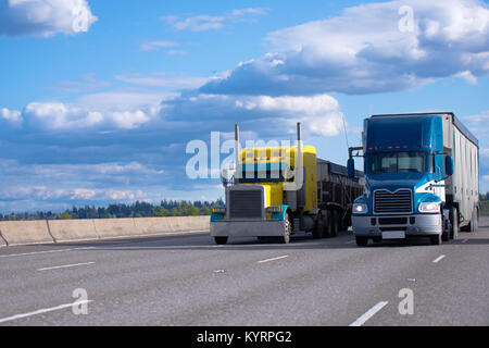 Zwei semi Trucks verschiedener Modelle und Hersteller, eine gelbe klassische amerikanische Semi Truck mit einem bulk Trailer und einen blauen moderne amerikanische Semi Truck Stockfoto