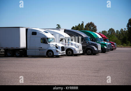 Farbenfrohe, moderne big Rigs Semi-Lkw und Anhänger verschiedener Marken und Modelle stehen in der Zeile auf einem Parkplatz von Truck Stop im Sonnenschein Stockfoto