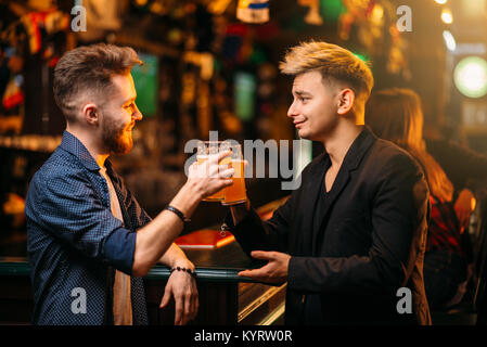 Zwei Männer an der Theke, hob die Gläser mit Bier für den Sieg in Spiel in einem Sport Pub , Freizeit der Fußball-Fans Stockfoto