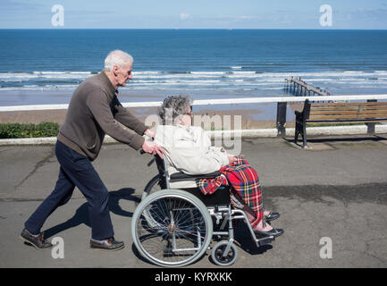 Älterer Mann drücken edlerly Frau im Rollstuhl an der Küste. Großbritannien Stockfoto