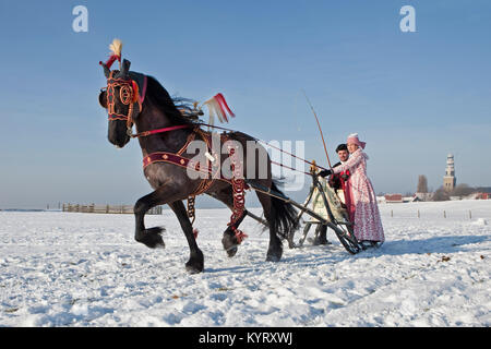 Die Niederlande, Hindeloopen, Antike mit Pferd und Schlitten und Friesenpferd. Mann und Frau in traditioneller Tracht. Winter. Stockfoto